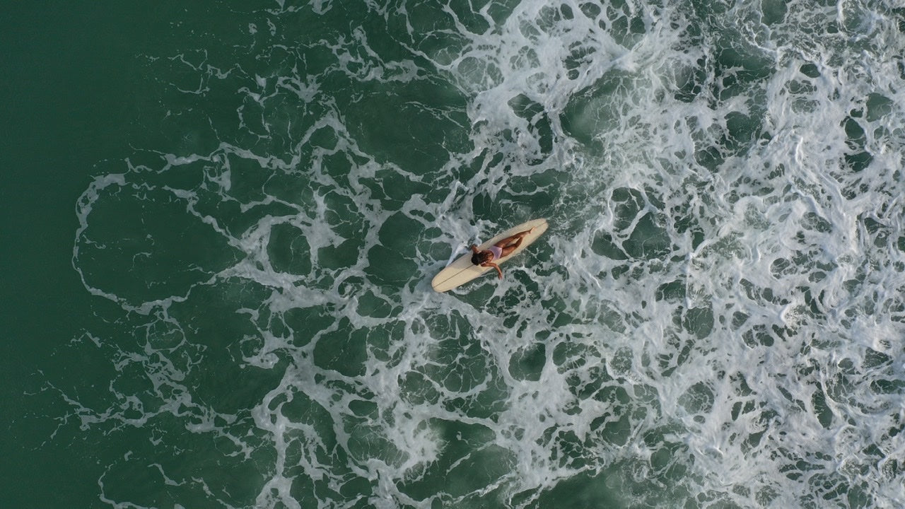 A dron shot of a woman paddling on lonboard in the ocean
