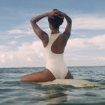 Krui Onepiece Surf Swimsuit in White with a long board on the water