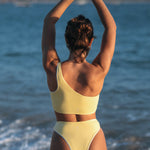 Woman wearing Ninefoot Studio Kongs one shoulder surf top in yellow– asymmetric cut Italian recycled fabric bikini top designed for movement in Bali