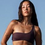 Woman wearing Ninefoot Studio Kongs one shoulder surf top in burgundy – asymmetric cut Italian recycled fabric bikini top designed for movement in Bali
