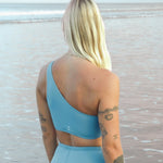 Woman wearing Ninefoot Studio Kongs one shoulder surf top in stone blue – asymmetric cut Italian recycled fabric bikini top designed for movement in Bali