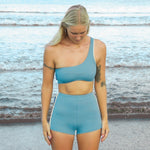 Woman wearing Ninefoot Studio Kongs one shoulder surf top in stone blue – asymmetric cut Italian recycled fabric bikini top designed for movement in Bali